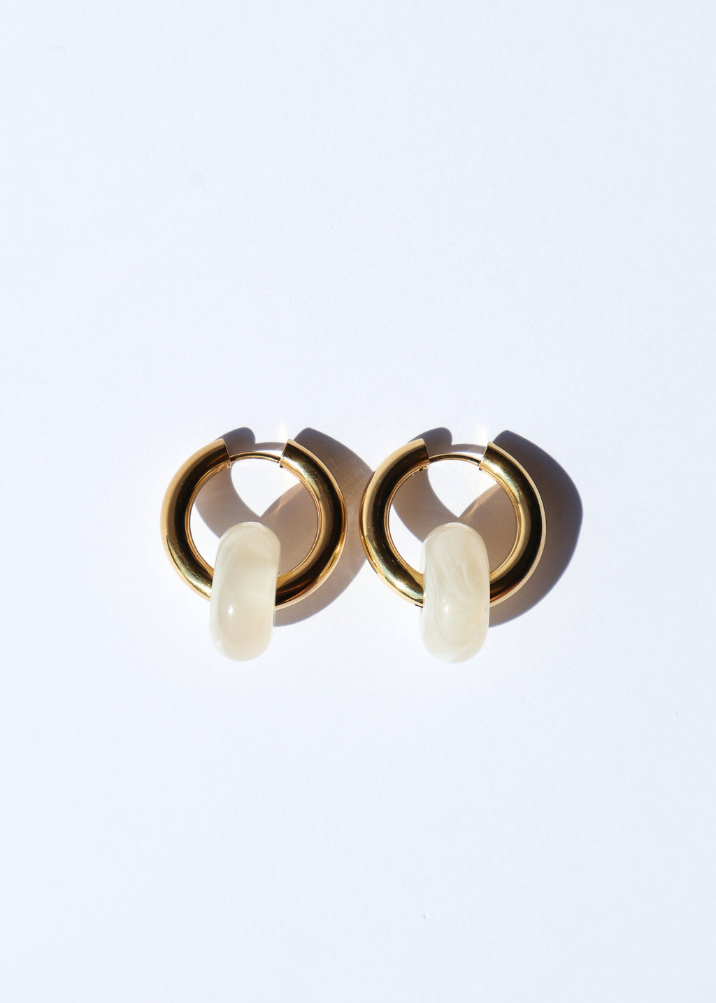 Boucles d'oreilles type créoles avec fermoir à charnière en acier inoxydable composées d'un anneau simple ainsi que d'une pièce en forme de donut en acétate coloré couleur vanille/beige