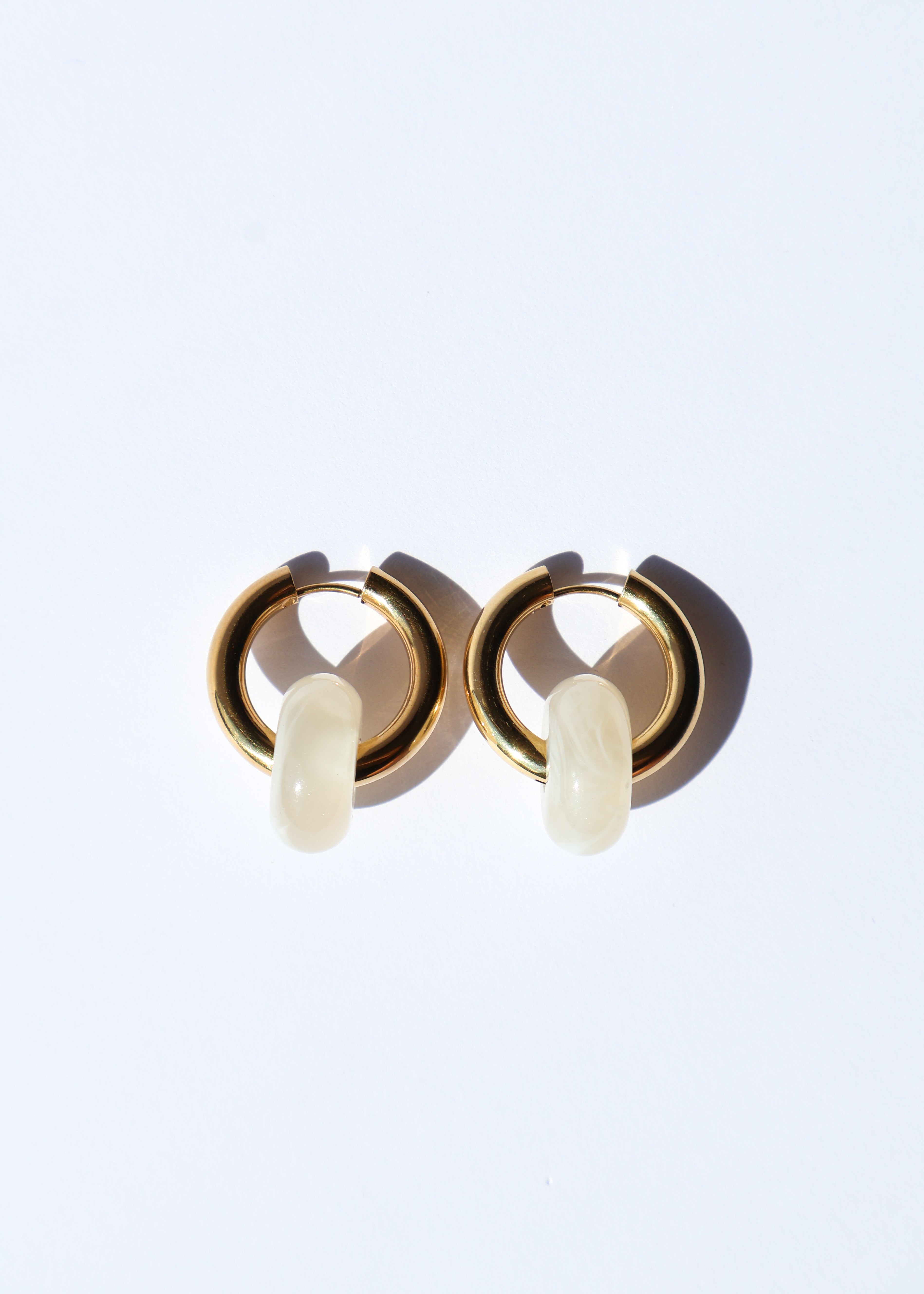 Boucles d'oreilles type créoles avec fermoir à charnière en acier inoxydable composées d'un anneau simple ainsi que d'une pièce en forme de donut en acétate coloré couleur vanille/beige