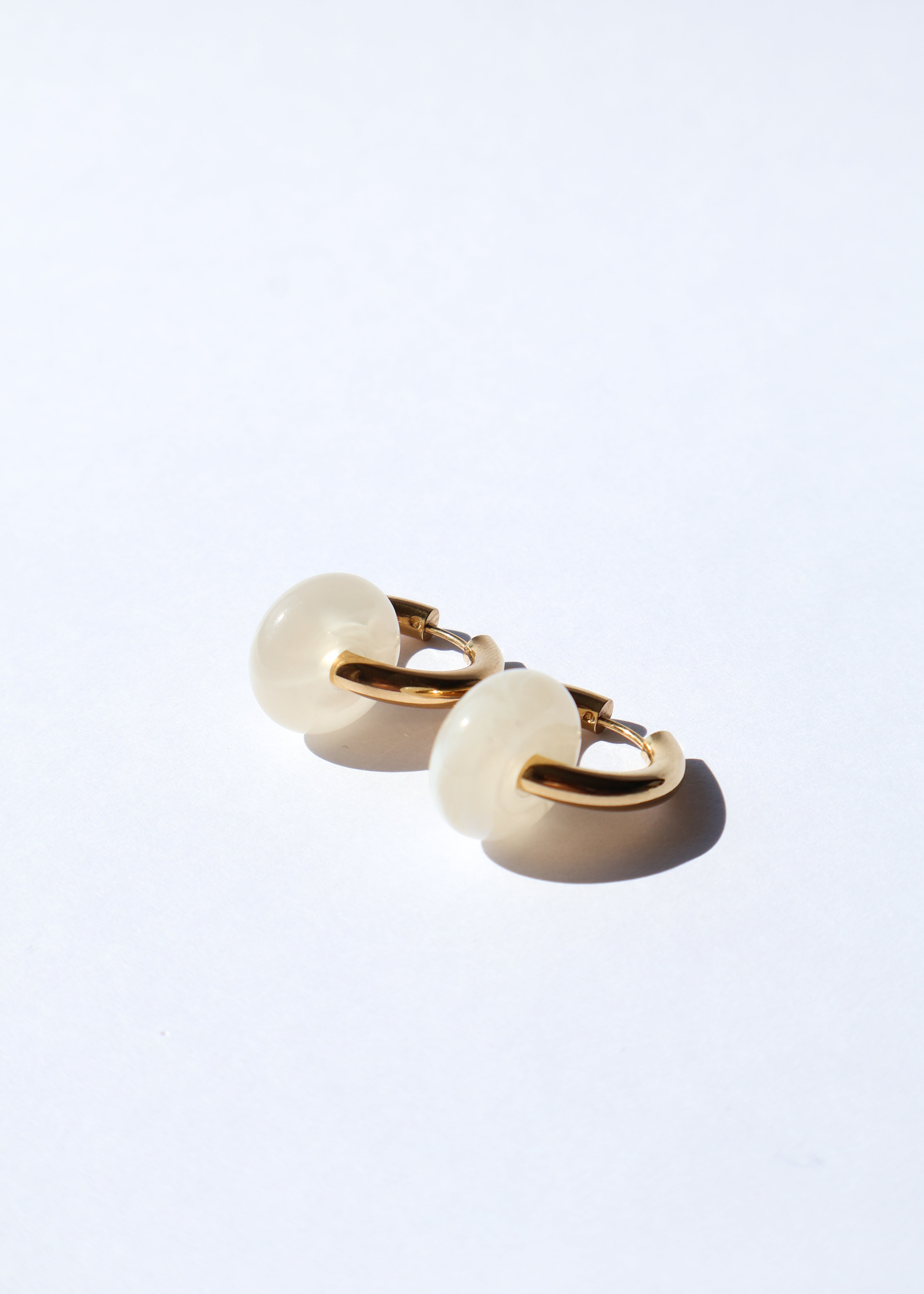 Boucles d'oreilles type créoles avec fermoir à charnière en acier inoxydable composées d'un anneau simple ainsi que d'une pièce en forme de donut en acétate coloré couleur vanille/beige