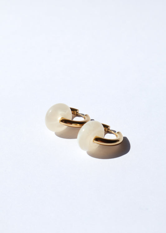 Boucles d'oreilles type créoles avec fermoir à charnière en acier inoxydable composées d'un anneau simple ainsi que d'une pièce en forme de donut en acétate coloré couleur vanille/beige